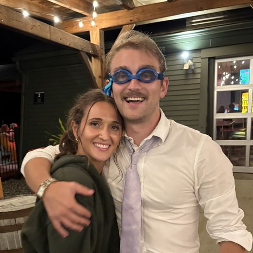 Alec wearing swim goggles and a tie with a friend