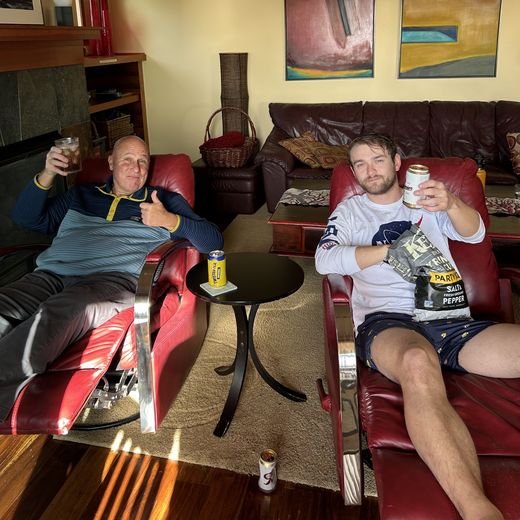 Alec and a friend kicking back in red recliners with drinks and chips