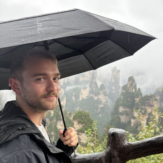Alec under an umbrella in front of misty mountain peaks